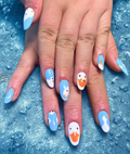 A close-up of manicured fingernails featuring a duck-themed nail art design with light blue and white backgrounds and orange beaks, shown on a textured blue surface with water droplets.
